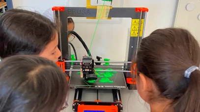Children watching a 3D printer create a bright green object.